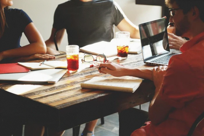 Title: Fig 6 - Description: Team discussing priorities around a table with laptops and notebooks